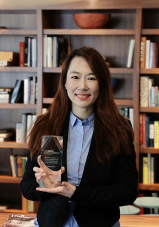 image of Tracy holding alumni award, backdrop of an office