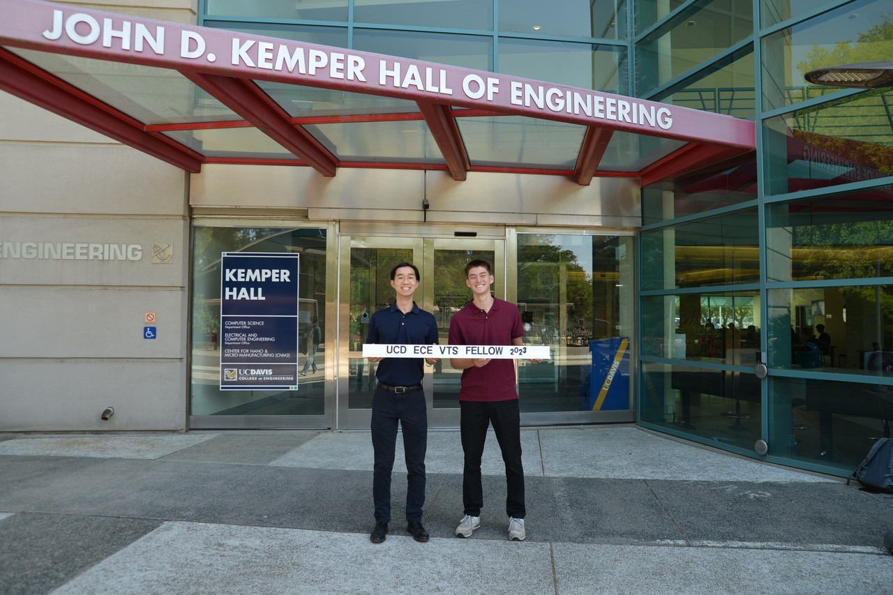 Two UC Davis ECE students hold a sign and stand near Kemper Hall