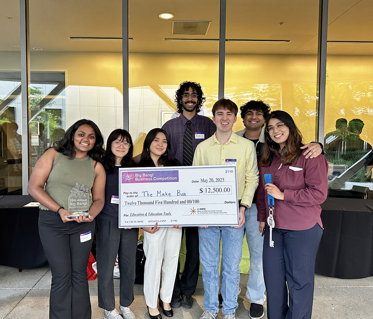 Group of students stand near glass windows holding a big check, clear award and key