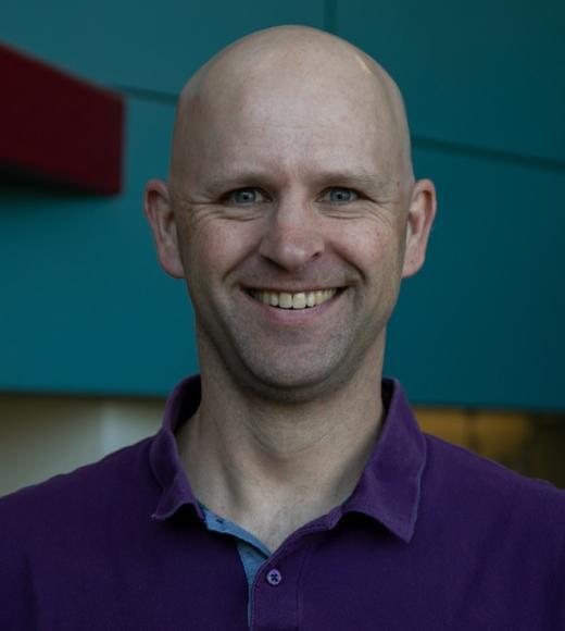 Middle aged white man with a blue polo shirt and bald head
