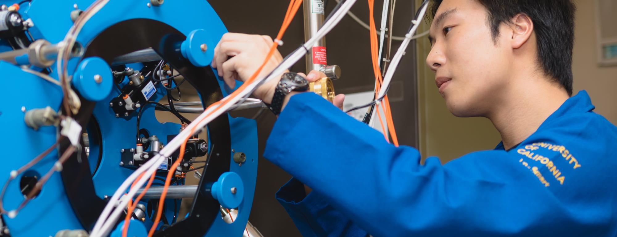 A student in a blue lab uniform working on a circular machine component