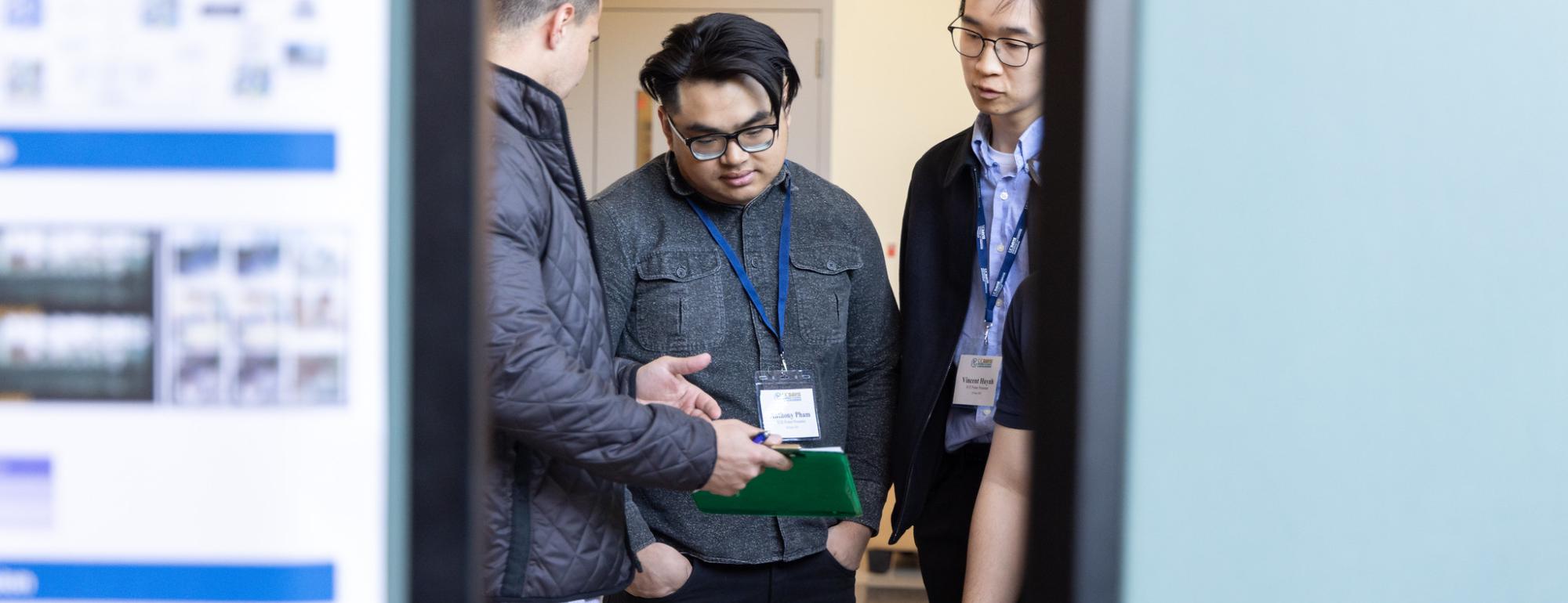 Three students are framed by research poster boards