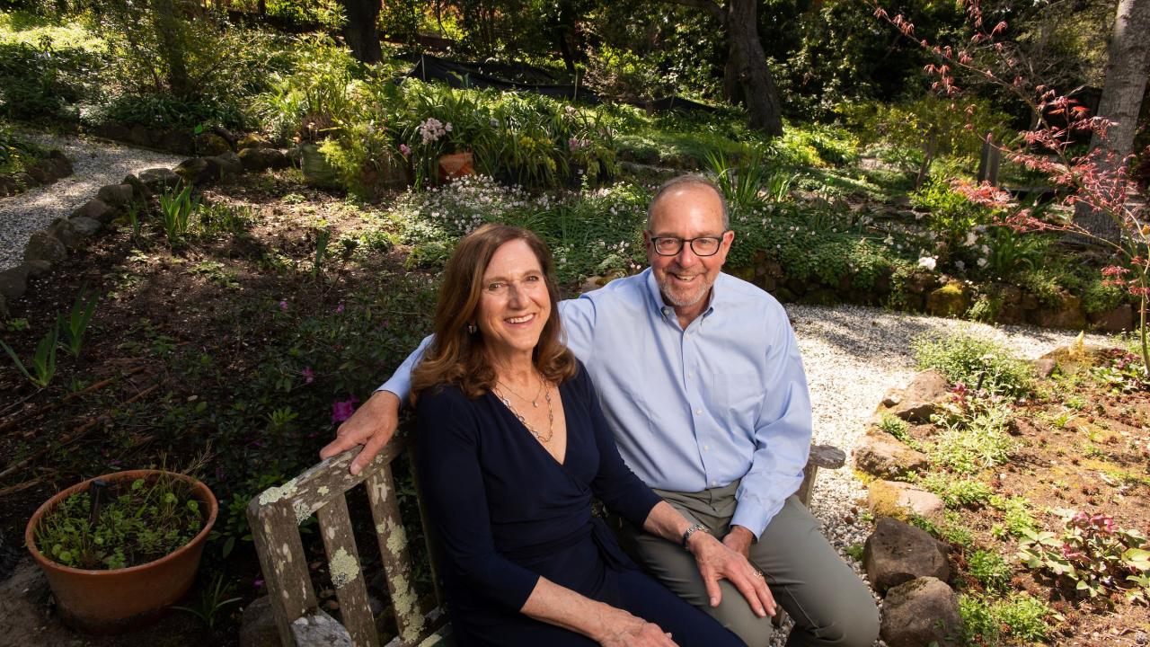 A man and women sit on a bench in a garden