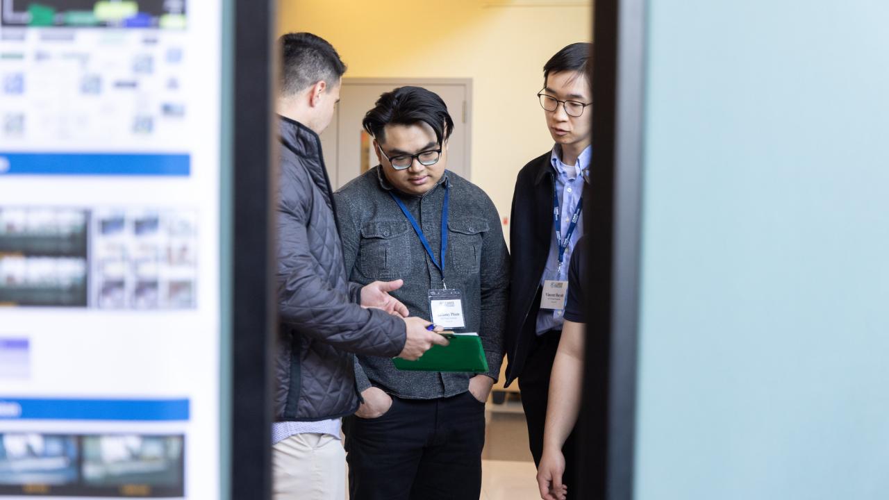 Three students are framed by research poster boards