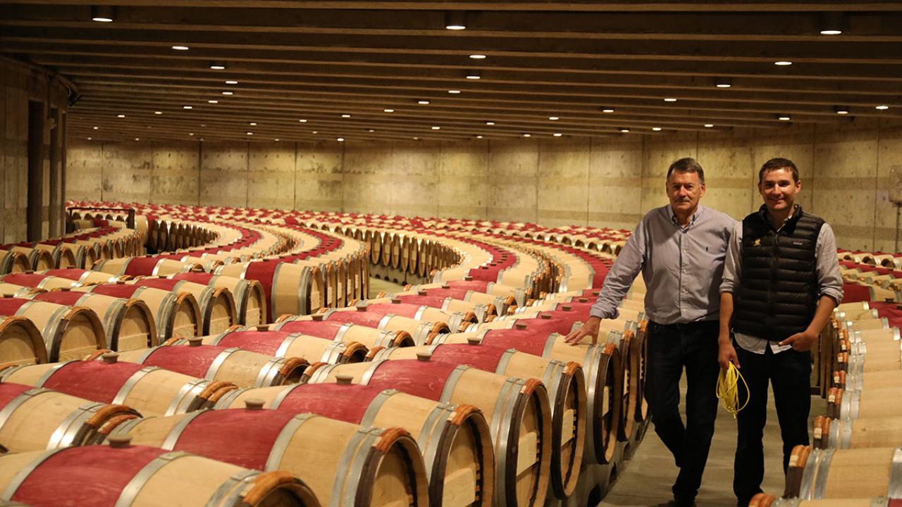Two people stand in a circular room with hundreds of barrels of wine spiraling around