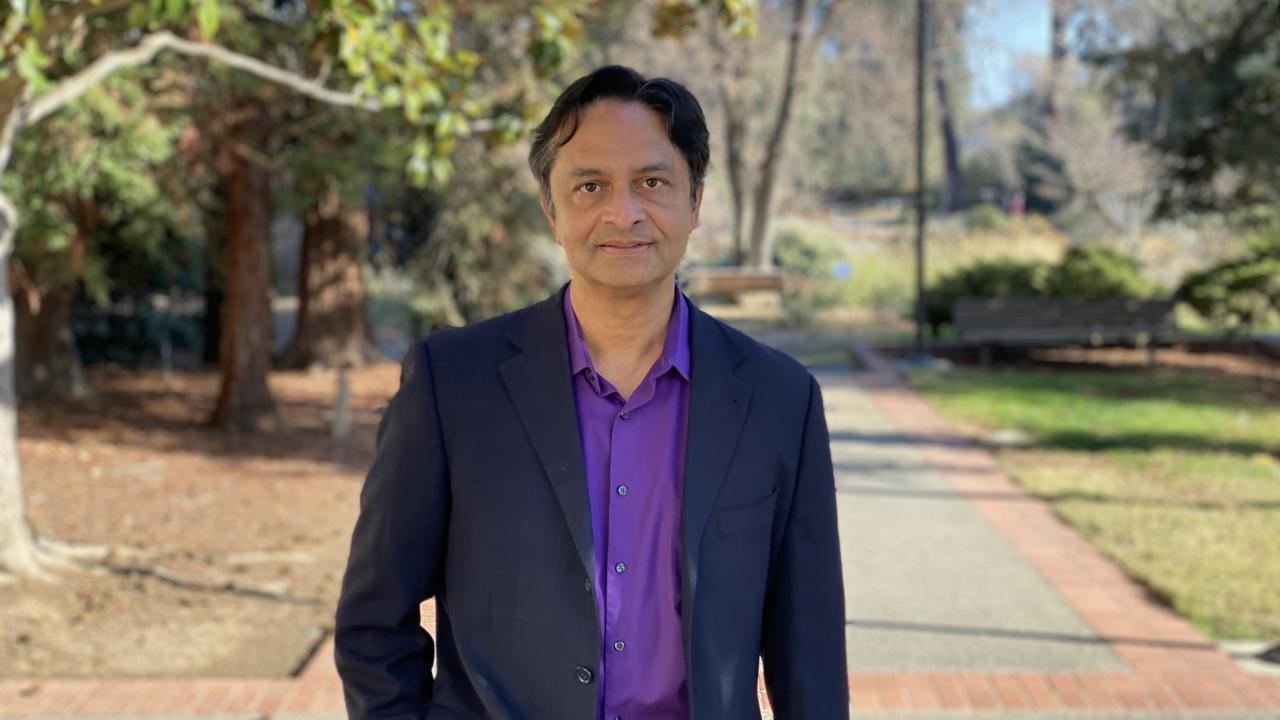 Middle aged man with a shirt and coat standing on a sidewalk near trees