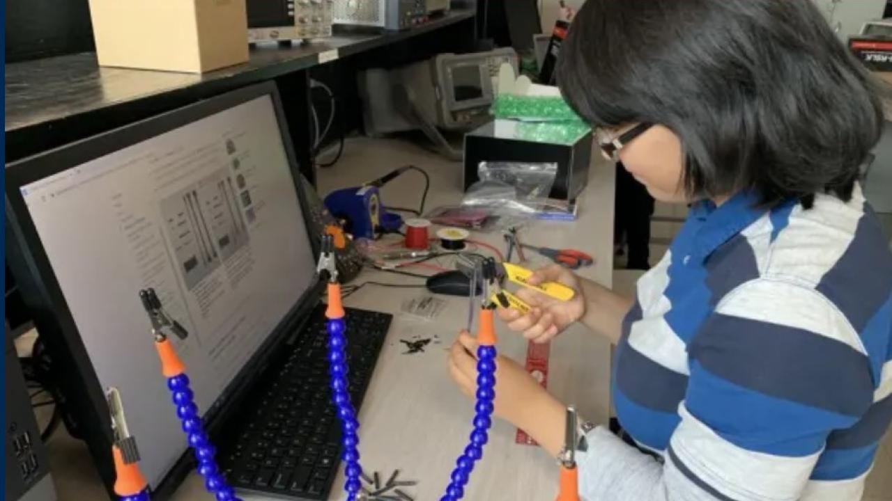 Young Asian woman tinkering with electronics in front of a computer