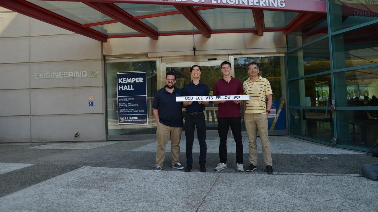 Two UC Davis ECE students and professors stand near a building with a red sign that says John D Kemper Hall of Engineering