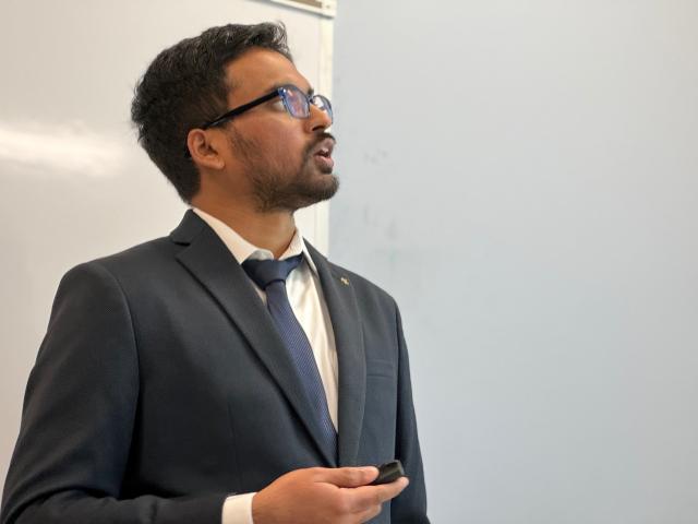A man wearing a suit and tie presents in a classroom