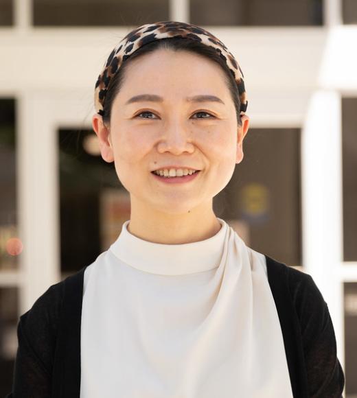 Jane Gu wearing a white blouse and black cardigan standing outdoors near a building on the UC Davis campus