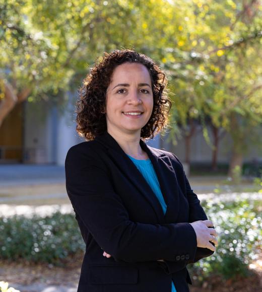 Radulaski in black blazer with arms crossed on sunlit campus pathway