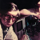 Two scientists wearing safety goggles work on a laser setup in a lab.