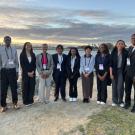 A group of Black students wearing nametags and lanyards stand on grass and sand
