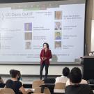 Person stands in front of a projector screen speaking to a crowd